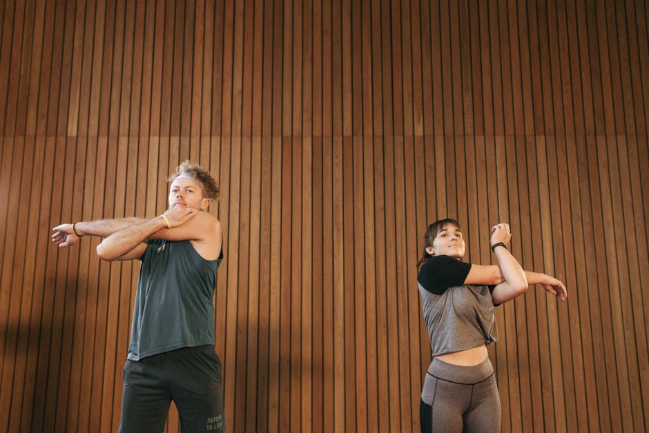 A man and a woman engage in stretching exercises indoors, emphasizing health and fitness.