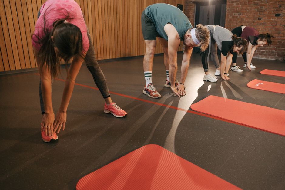 A diverse group of adults stretching on mats during a gym workout session.