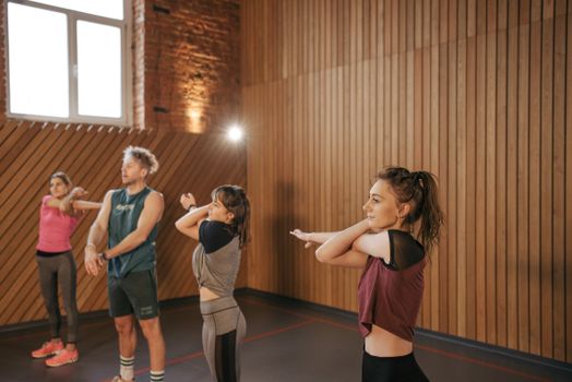A group of adults engaging in stretching exercises during a fitness class in a wooden-paneled gym.