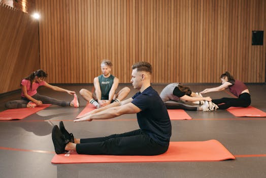 A diverse group of adults practicing yoga stretches on mats in a wooden studio.