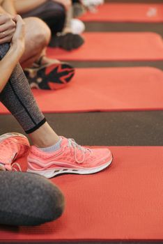 Close-up photo of athletes in leggings and sneakers on red yoga mats.