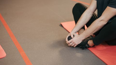 Adult man stretching on a red yoga mat indoors, focusing on flexibility and fitness.