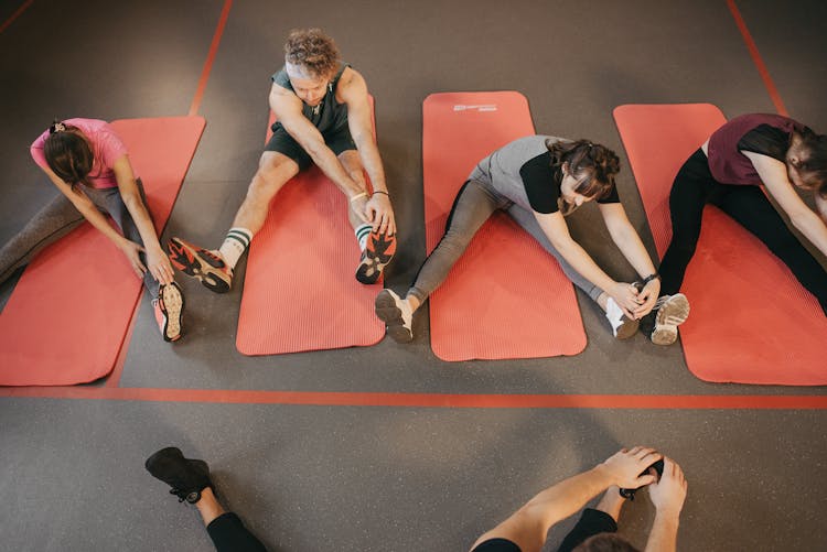 A Group Of People Sitting On Mats Stretching