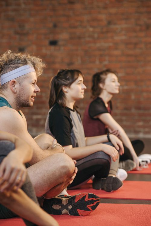 Free Three adults in a gym setting during a yoga session, seated on red mats. Stock Photo