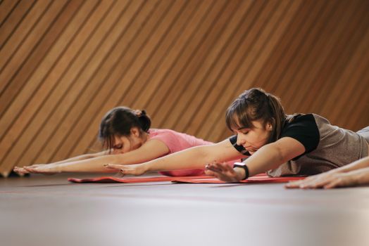 Two women are stretching on yoga mats indoors, promoting health and fitness.