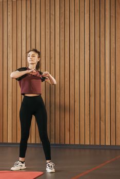 Woman in athletic wear stretches indoors against wooden panels, embracing a healthy lifestyle.