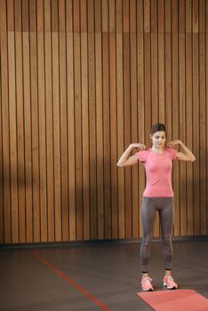 Young woman in sportswear doing shoulder rotations indoors on a yoga mat.