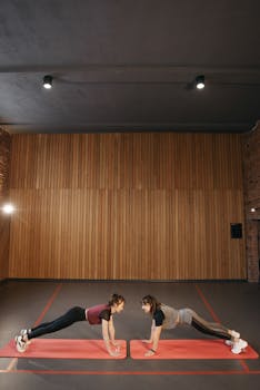 Two women engaged in a workout session indoors on red yoga mats. Fitness and teamwork.