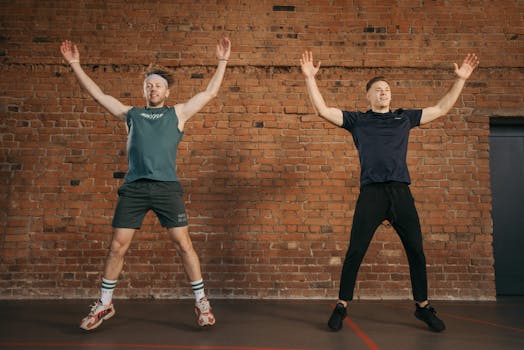 Two men performing jumping jacks in a gym setting, showcasing fitness and energy.
