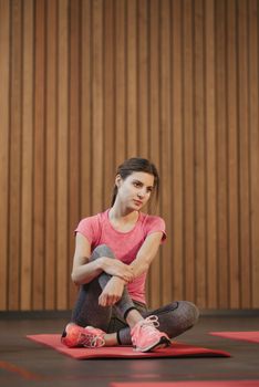 Young woman sitting on a yoga mat indoors, wearing a pink shirt during a workout session.