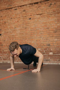 Man in a gym performing push-ups against a brick wall.