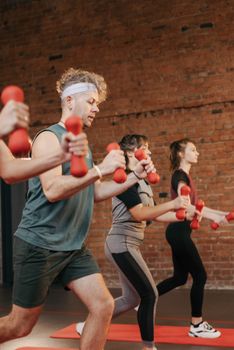 Diverse group exercising with dumbbells in an indoor gym setting, promoting healthy lifestyle.