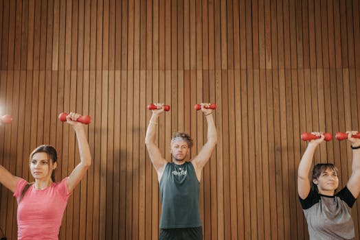 Three adults exercising with dumbbells in fitness class, promoting a healthy lifestyle.