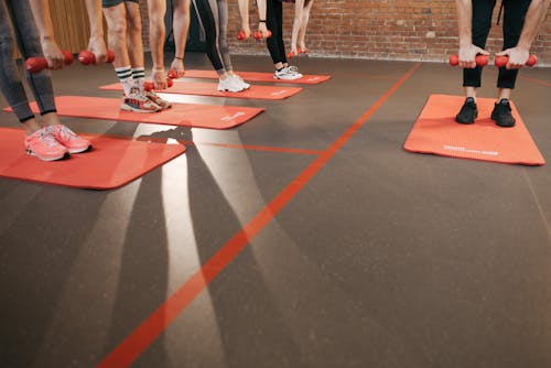 People Standing on a Yoga Mat Exercising with Dumbbells