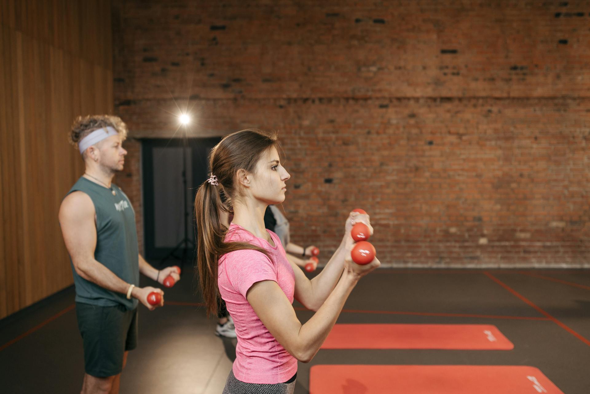 Group of adults exercising indoors with dumbbells, focused on fitness and health.