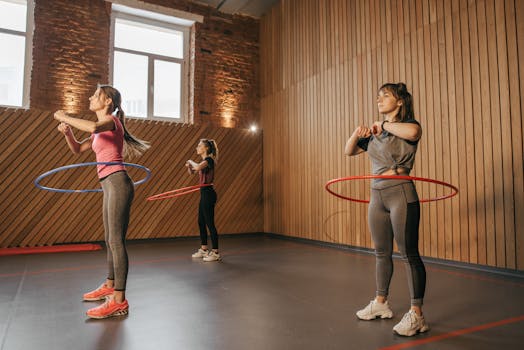 Three women exercising with hula hoops in a wooden-paneled gym.