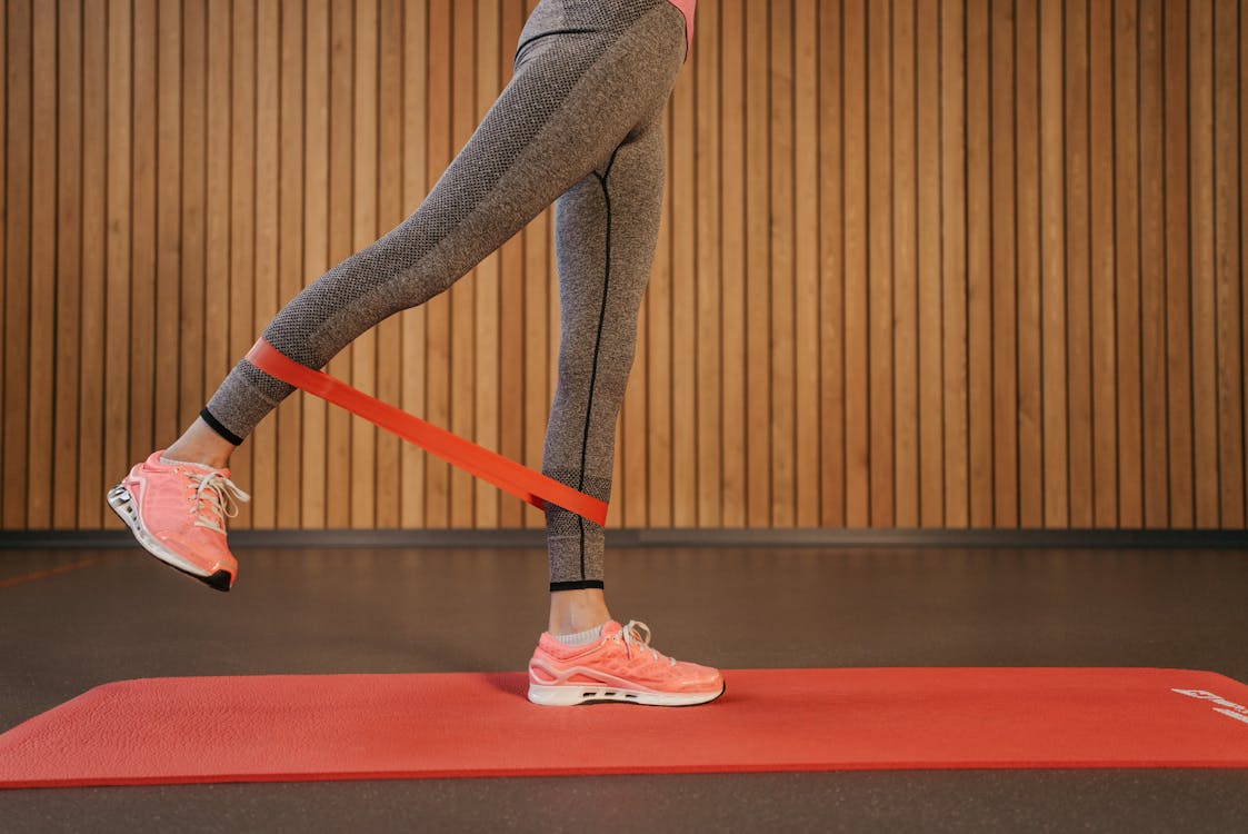 Free A woman performing leg exercises using a red resistance band on a yoga mat indoors. Stock Photo