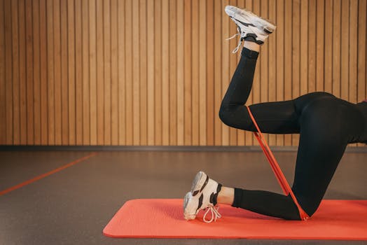 Woman in activewear working out indoors with resistance band on yoga mat, focusing on legs.
