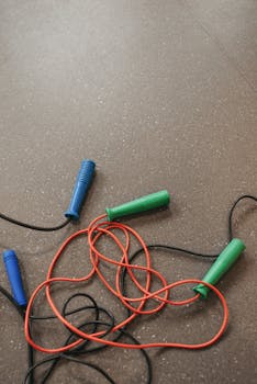 Tangled jump ropes with blue and green handles on textured gym floor.
