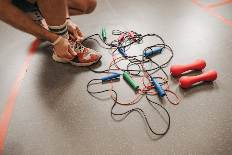 A Man Tying His Shoe Lace Beside Jump Ropes On The Floor