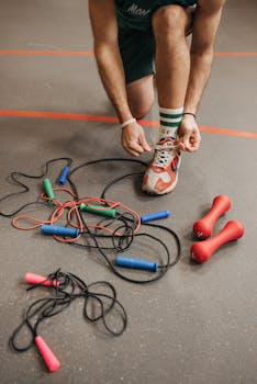 Close-up of gym equipment and runner tying shoelaces, ready for a workout.