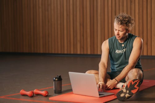 Man Sitting on Exercise Mat While Using a Laptop