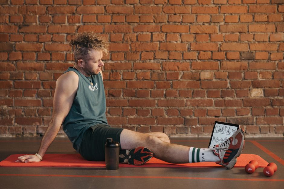 Athletic man sitting and resting on a mat in an urban gym, with a tablet and weights visible.