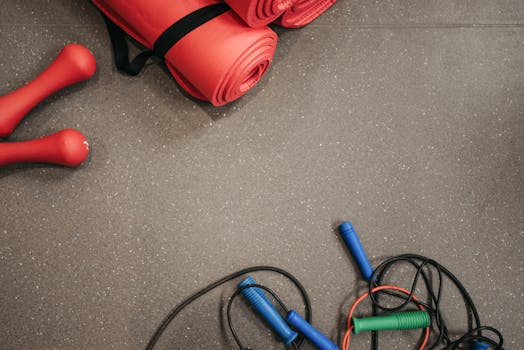 Red yoga mats, dumbbells, and jump ropes on a gym floor.