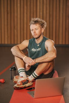 Man resting on a yoga mat after workout with a laptop nearby