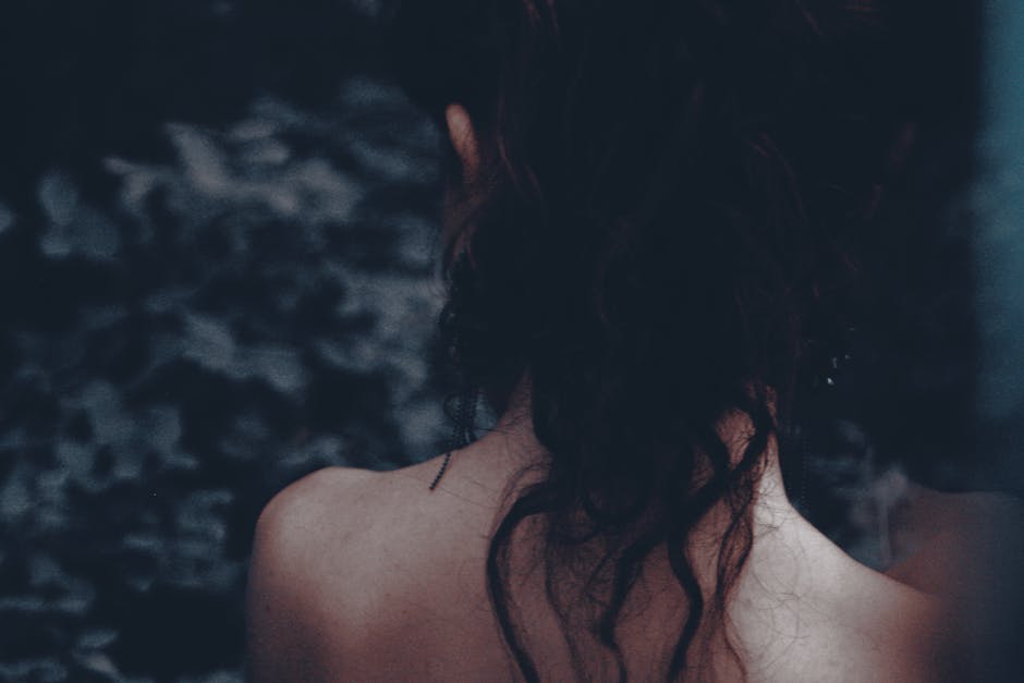 Artistic portrait of a woman seen from behind, highlighting her hair and bare shoulders in a moody setting.