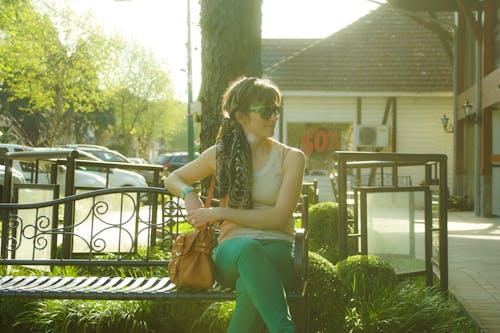 Free Woman in Brown Tank Top Sitting on Black Bench Beside Tree Stock Photo