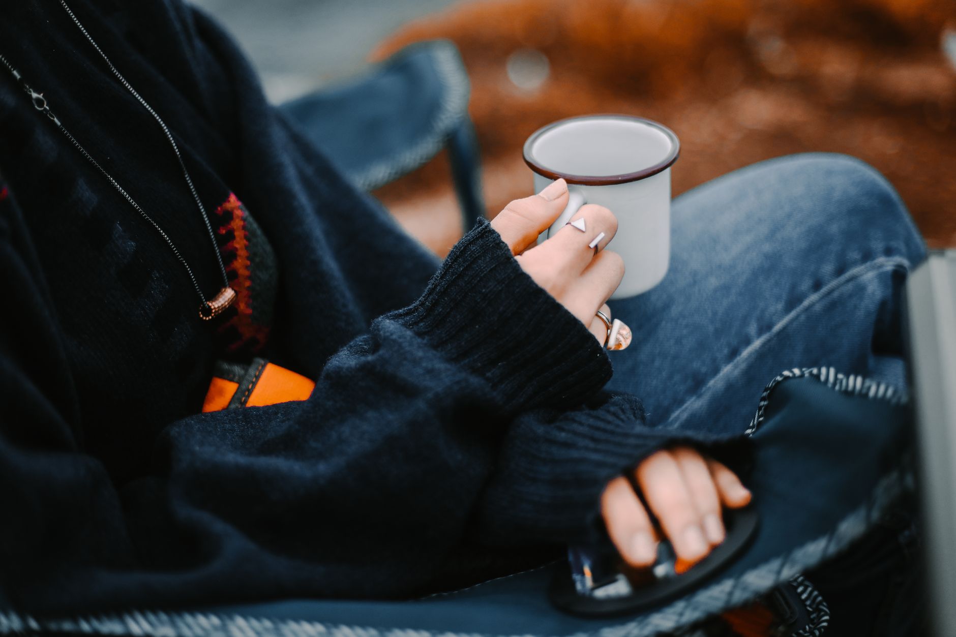 Person sitting outdoors in cozy sweater, holding warm cup, creating a serene moment.