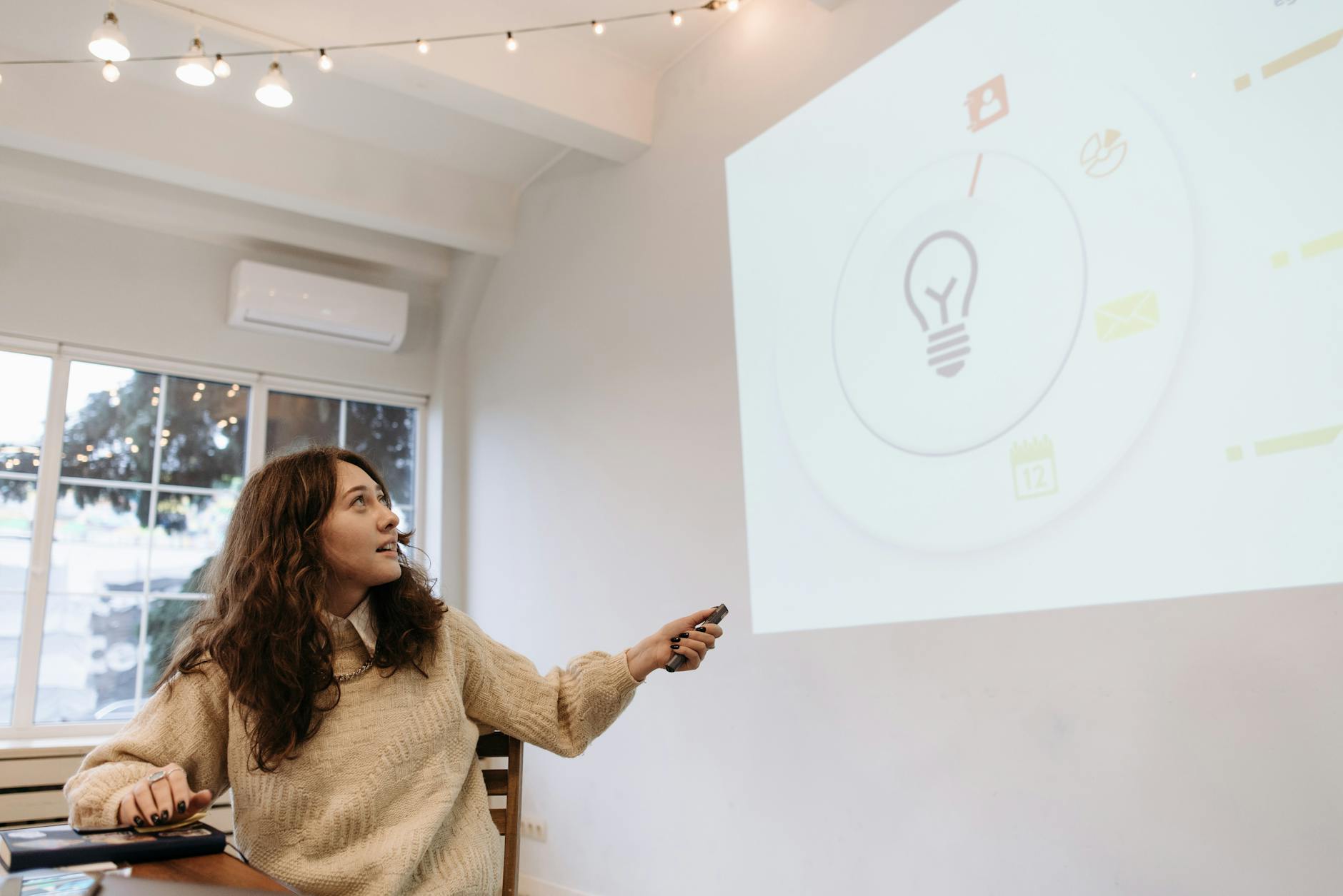 Young woman giving a business presentation, pointing at a screen in a modern office setting.