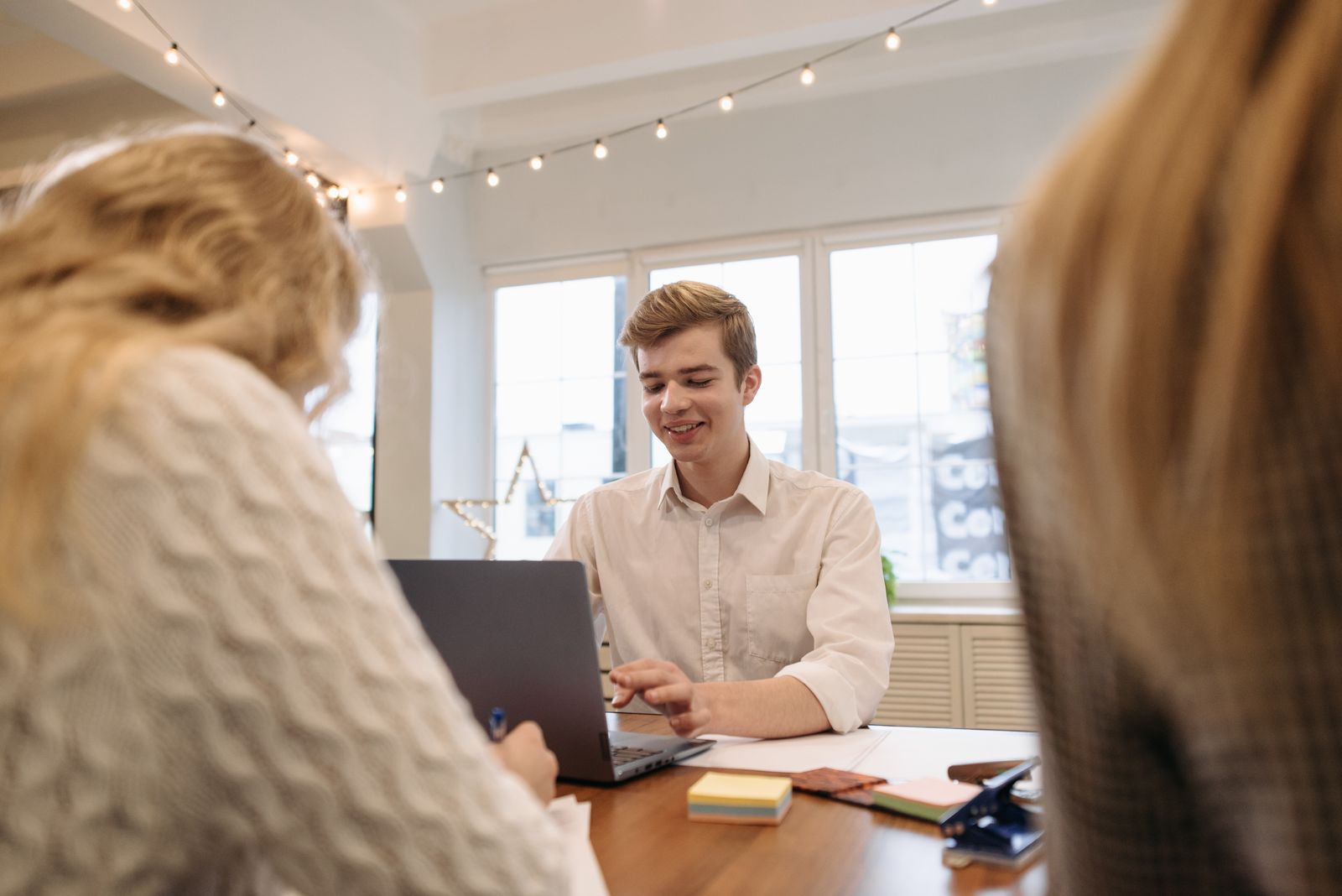 Free A young adult working on a laptop in a stylish office decorated with string lights provides a modern and professional ambiance. Stock Photo