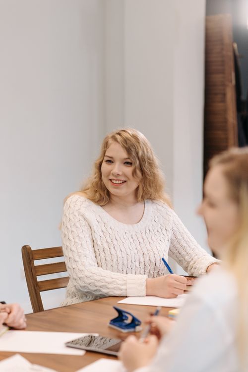Free Smiling young woman in a white knitted sweater participating in a meeting, creating a positive atmosphere. Stock Photo