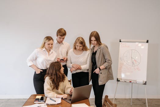 A group discussing a project around a laptop in a modern office setting.