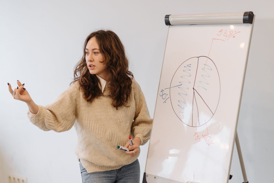 Free Woman gives presentation with pie chart on whiteboard, explaining data analysis. Stock Photo