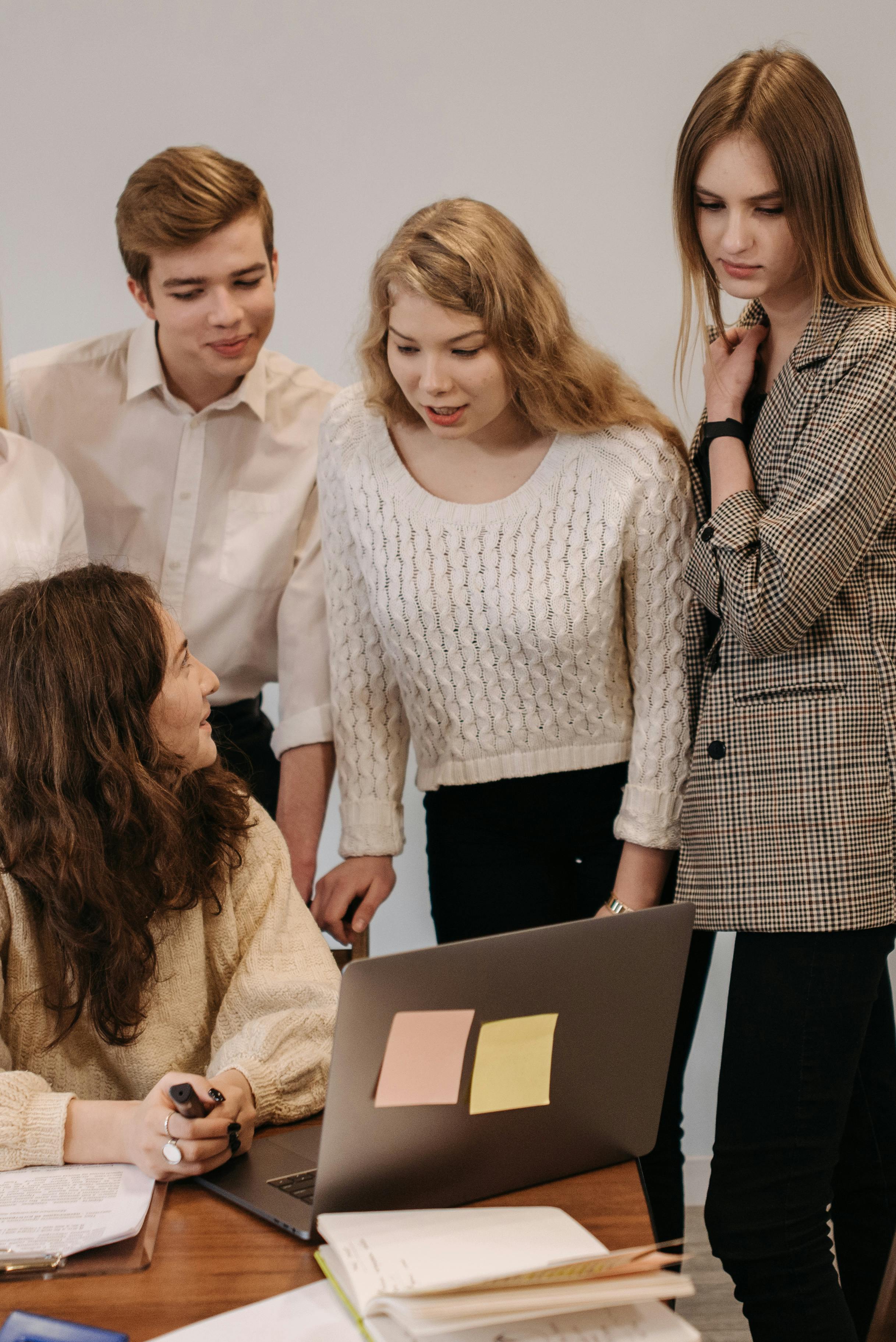 a group of young people talking and looking at a laptop screen