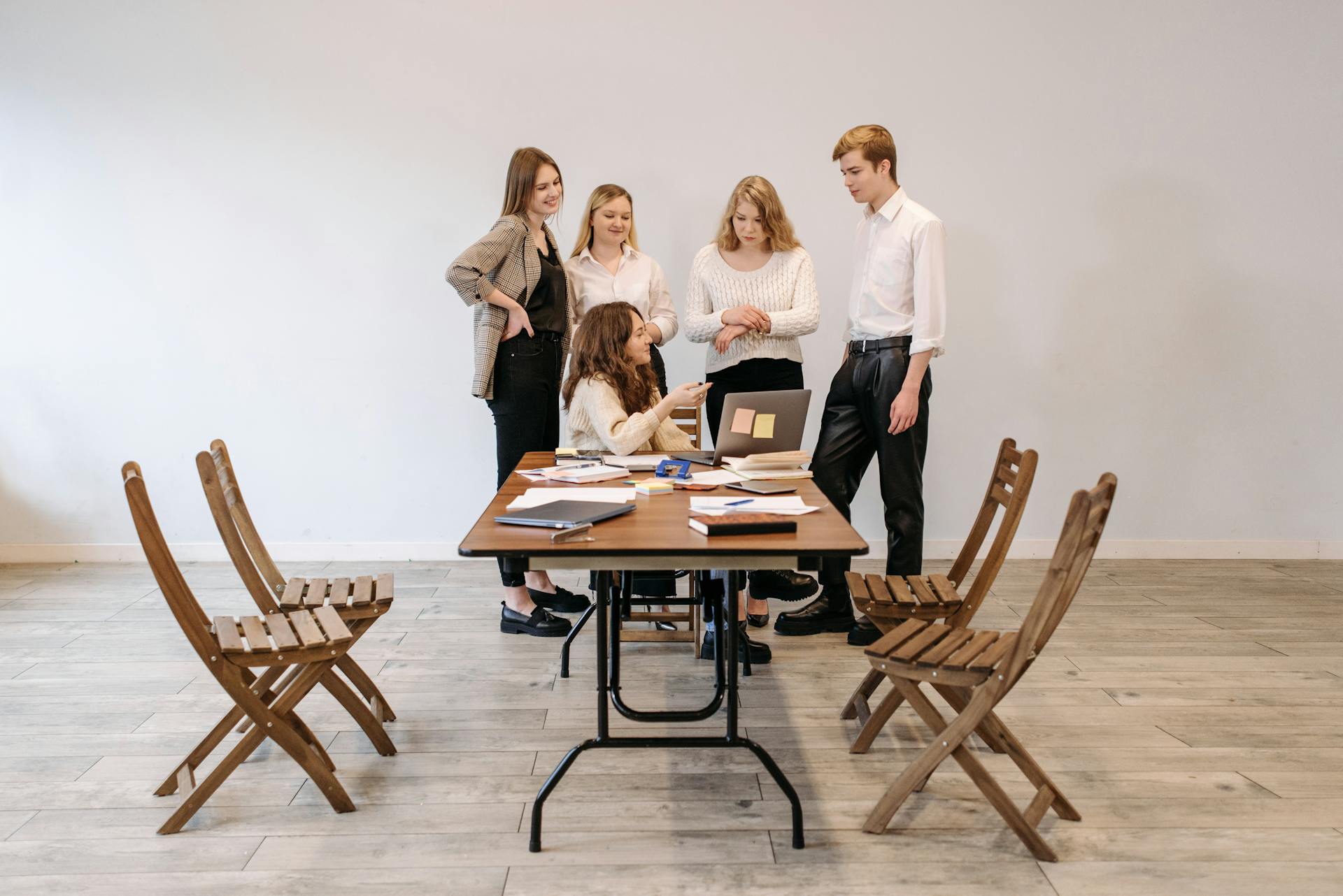 A group of young professionals collaborate in a modern meeting room around a laptop.