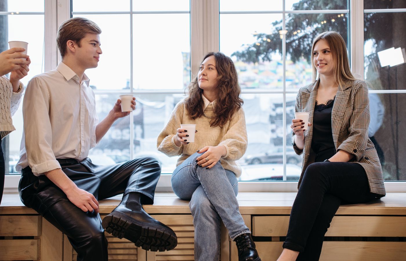 Three friends enjoying coffee together indoors by a large window.