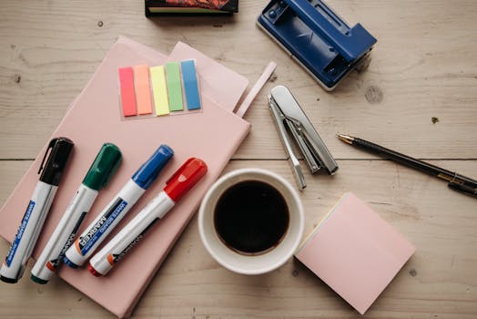 Flat lay of office supplies with coffee, markers, and notebooks on a wooden desk.