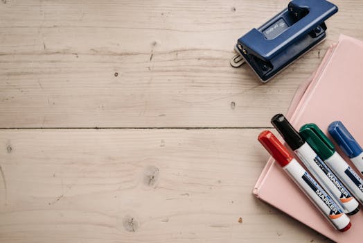 Top view of colorful markers and a blue stapler on a wooden desk with ample copy space.