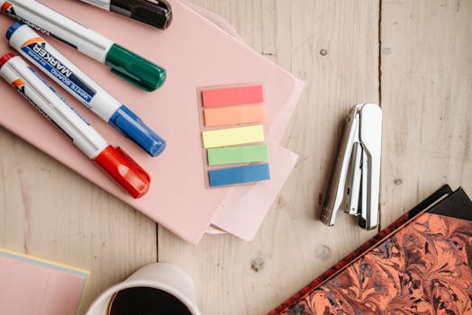 A flat lay of vibrant office supplies including markers, sticky notes, and a stapler on a wooden desk.