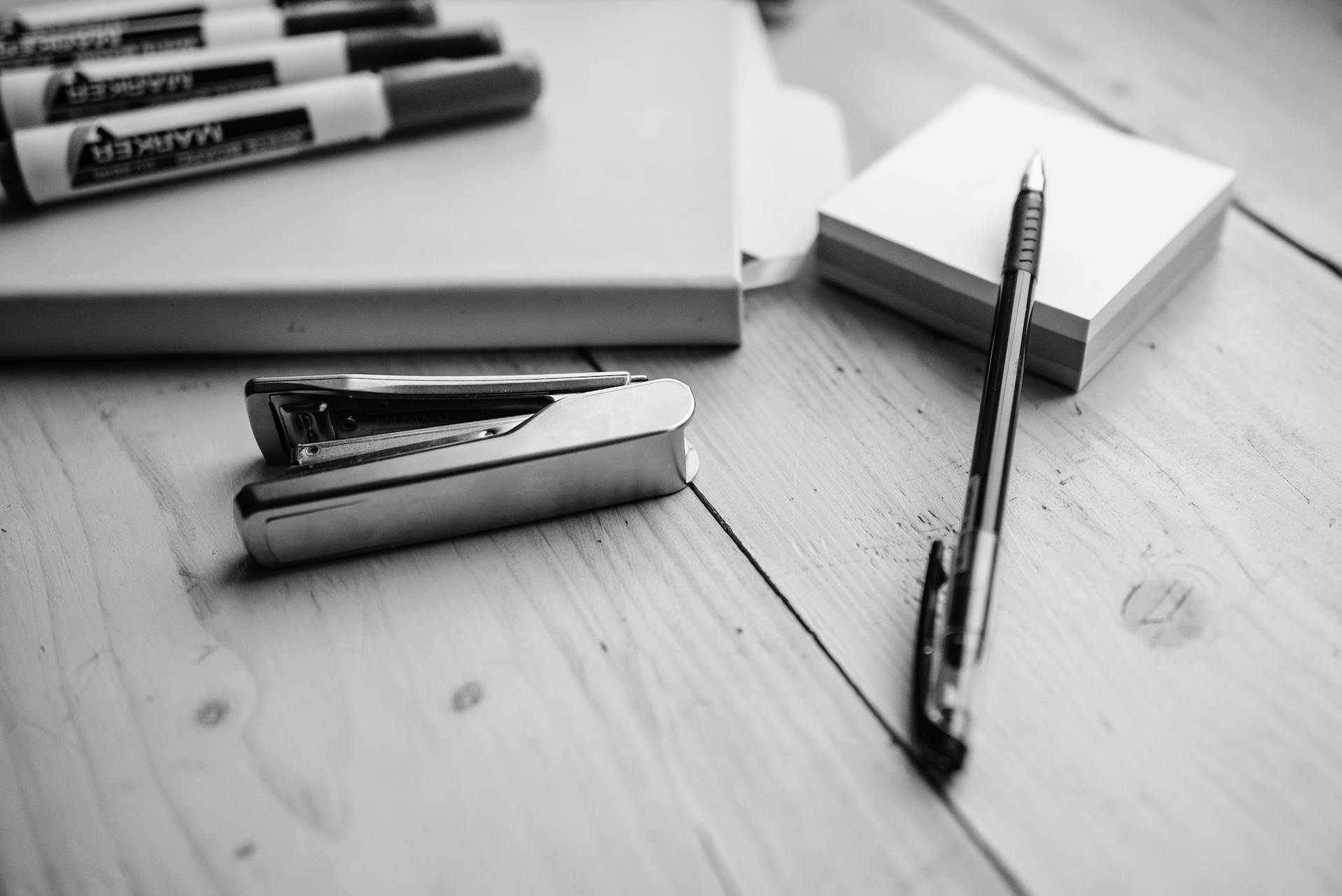 Grayscale Photo of a Stapler Near the Pen