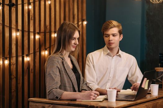 Two young adults having a conversation in a cozy cafe, using a laptop.