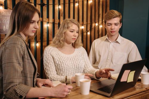 Free Three young adults in a casual setting collaborating over coffee and laptops indoors. Stock Photo