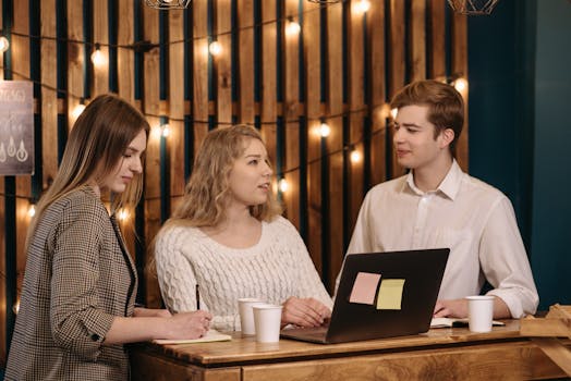 A group of young adults engaging in a discussion at a wooden table with a laptop, creating a warm and inviting atmosphere.
