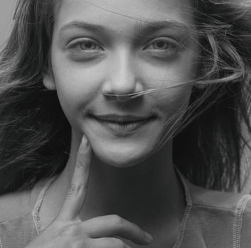 Grayscale close-up portrait of a smiling girl with hair flowing and finger pointing.