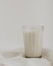 Faceted glass of cold fresh cow milk placed on white fabric against light wall