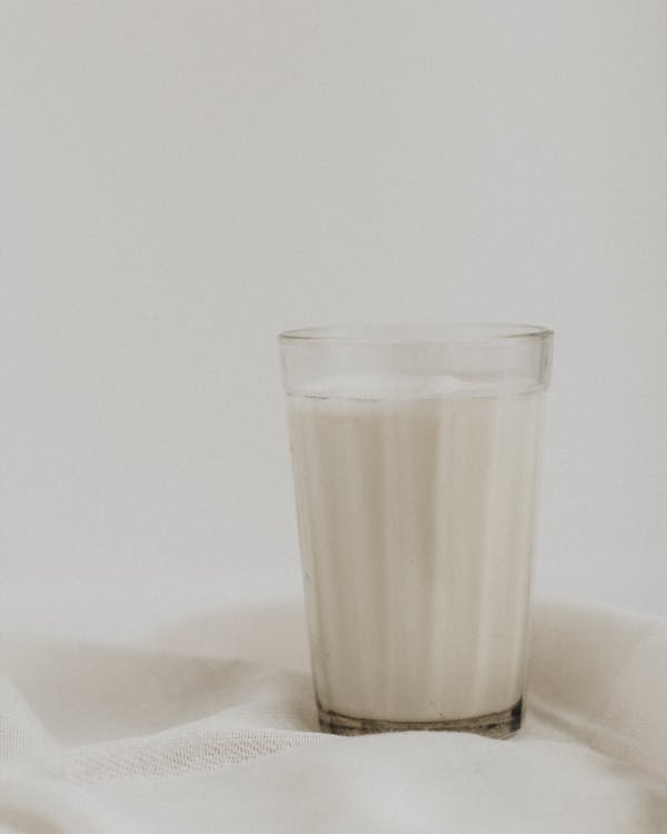 Faceted glass of cold fresh cow milk placed on white fabric against light wall
